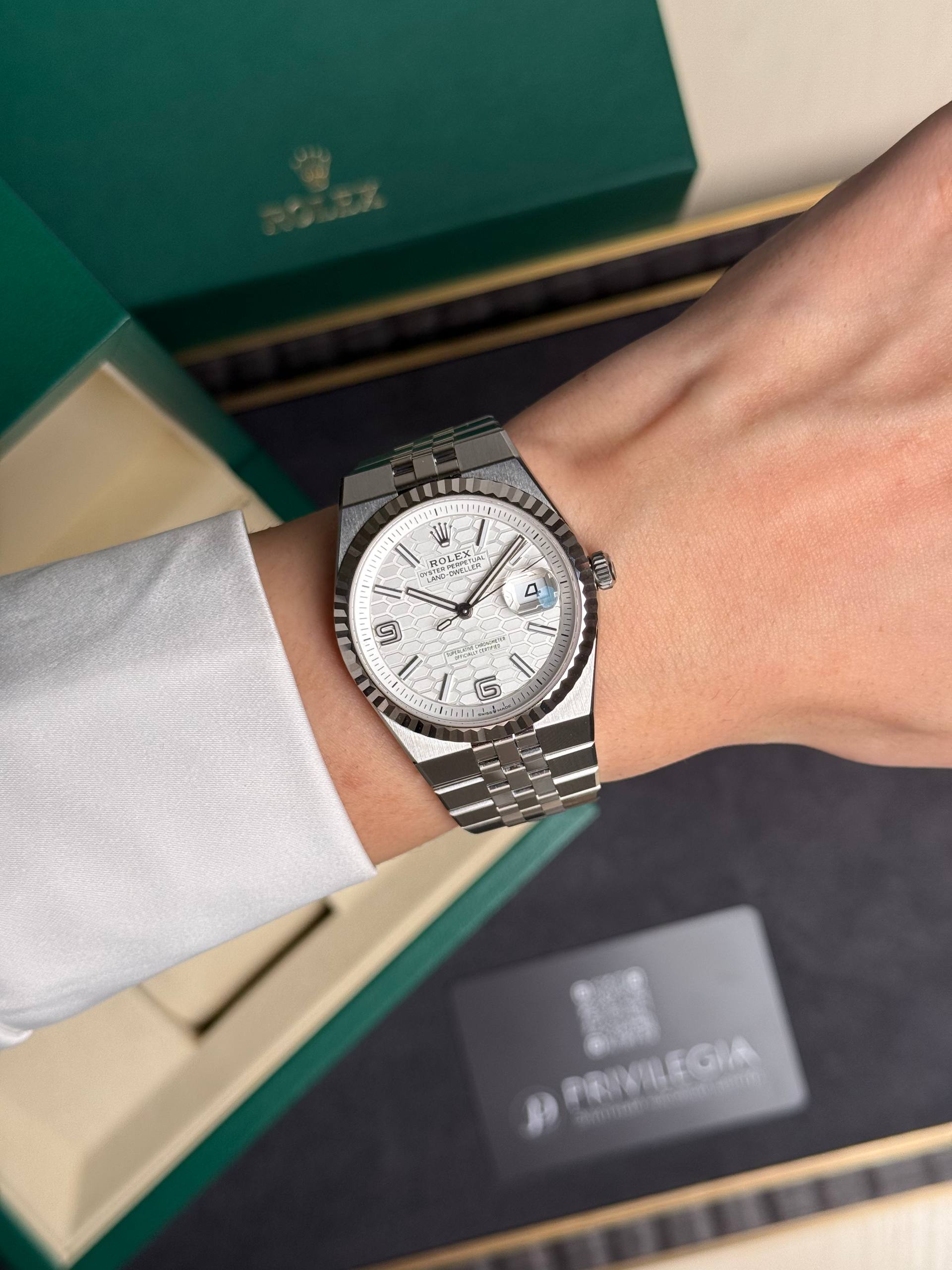 Stainless steel Rolex watch with a fluted bezel and date window worn on the wrist, with a green Rolex box in the background.