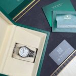 Rolex watch in beige display box with green outer box, accompanied by green booklet and card.