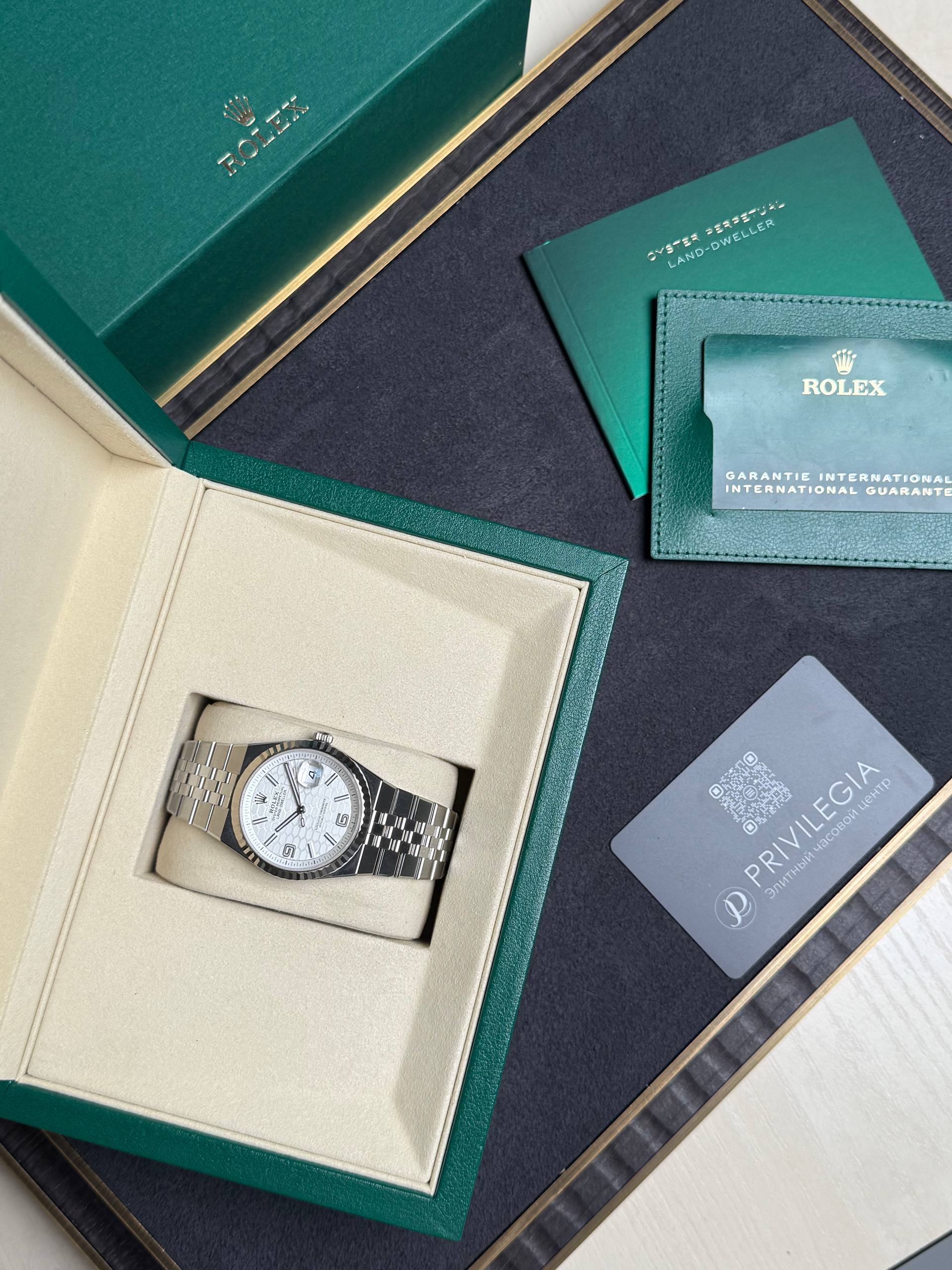 Rolex watch in beige display box with green outer box, accompanied by green booklet and card.