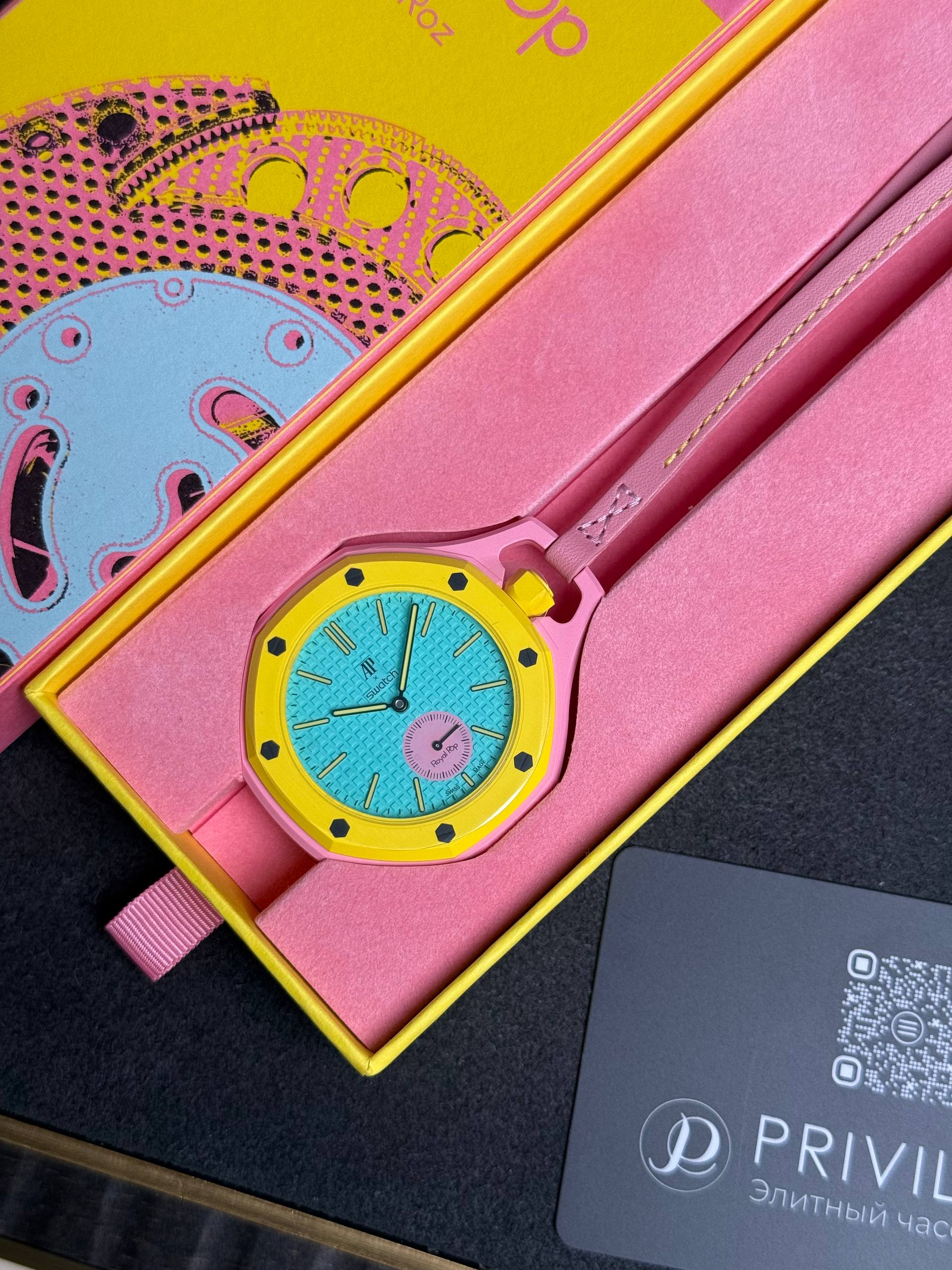 Colorful wristwatch in a pink and yellow box with a turquoise dial and yellow bezel, partially tucked open in packaging.