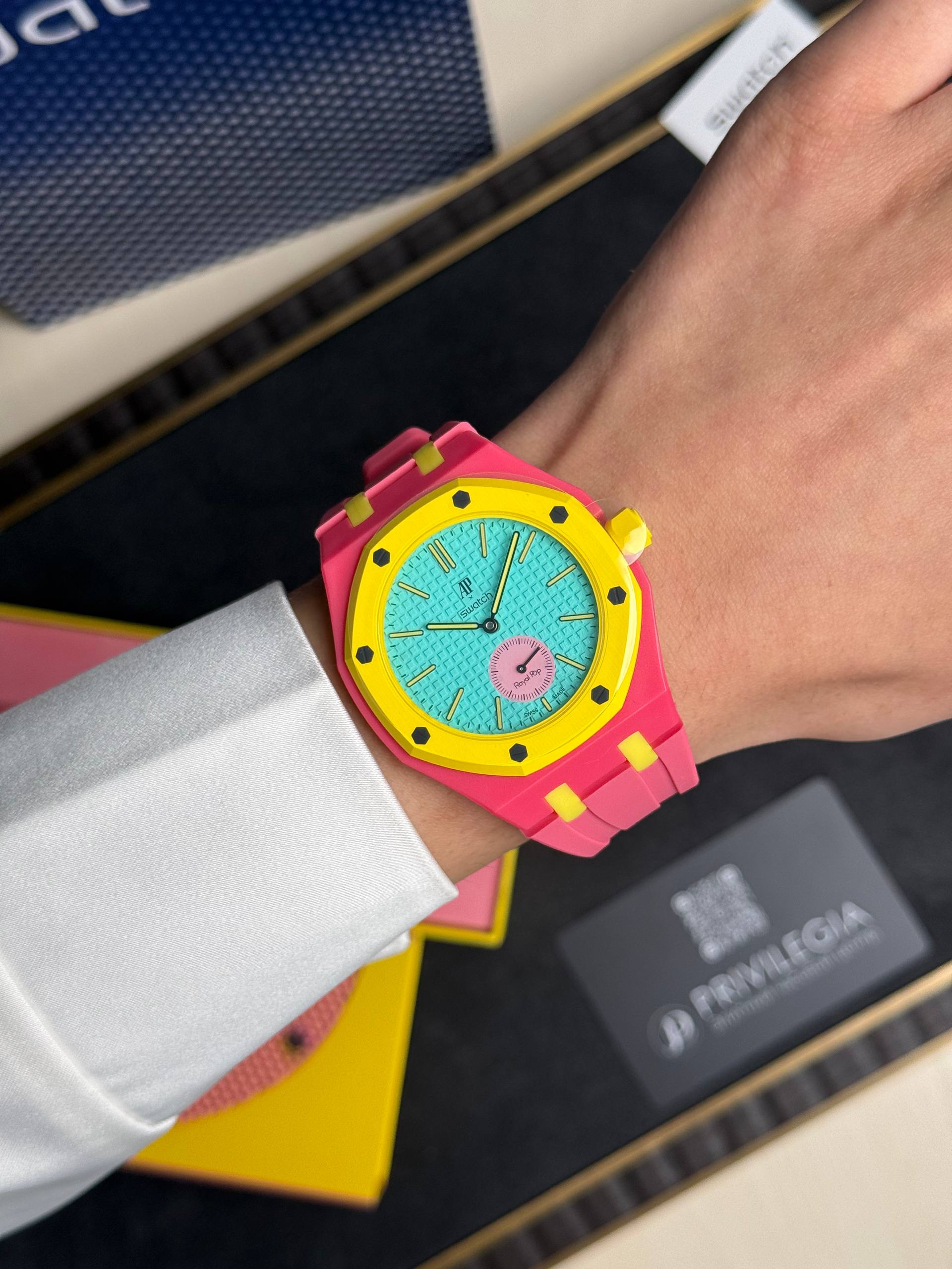 Bright pink wristwatch with a yellow bezel and turquoise dial on a person’s wrist