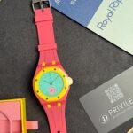 Bright pink Swatch watch with a turquoise dial and yellow bezel on a dark surface.