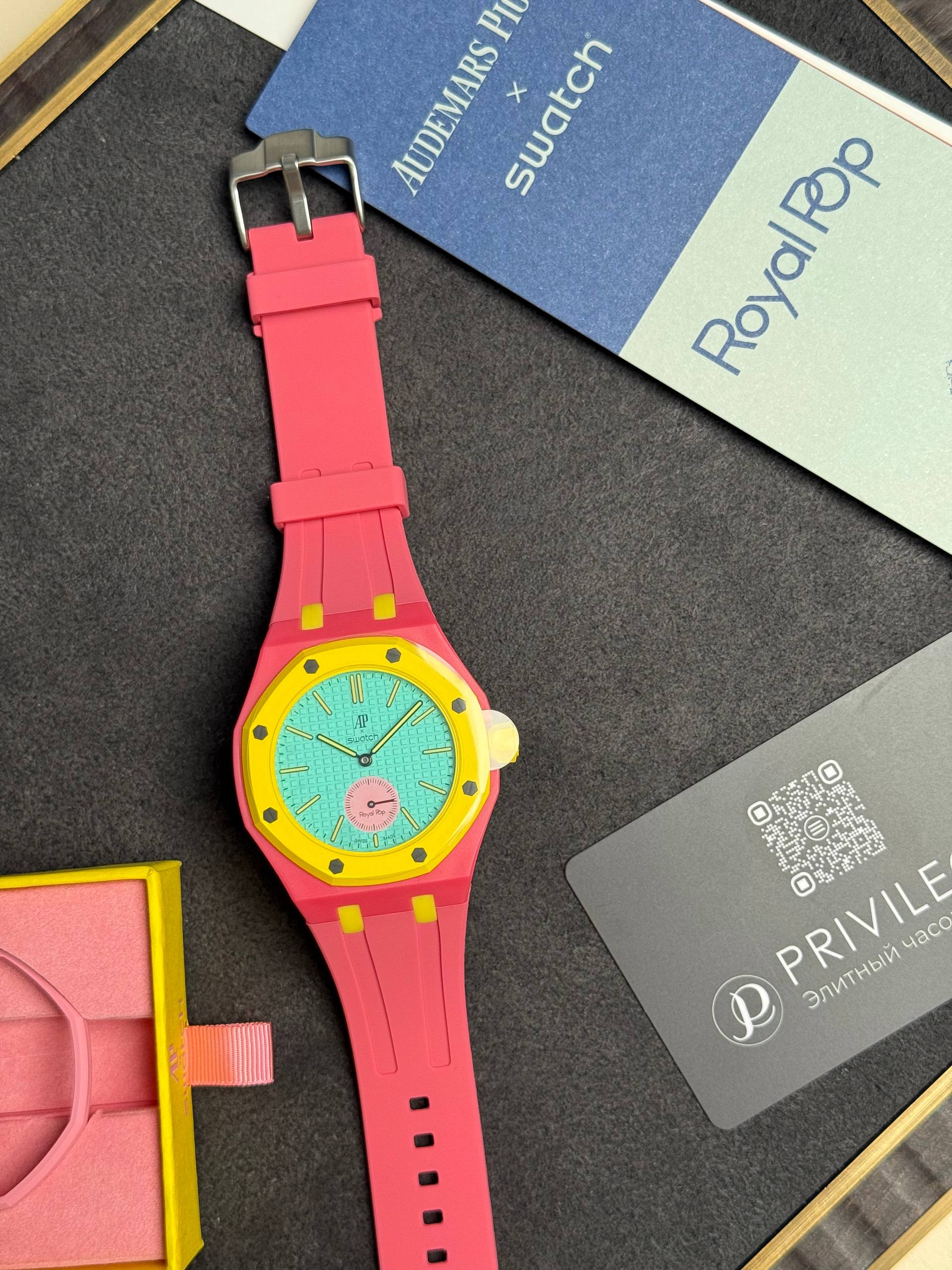 Bright pink Swatch watch with a turquoise dial and yellow bezel on a dark surface.