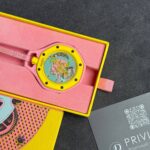 Swatch wristwatch in pink and yellow packaging; yellow bezel, pink band, in an open pink foam-lined box.