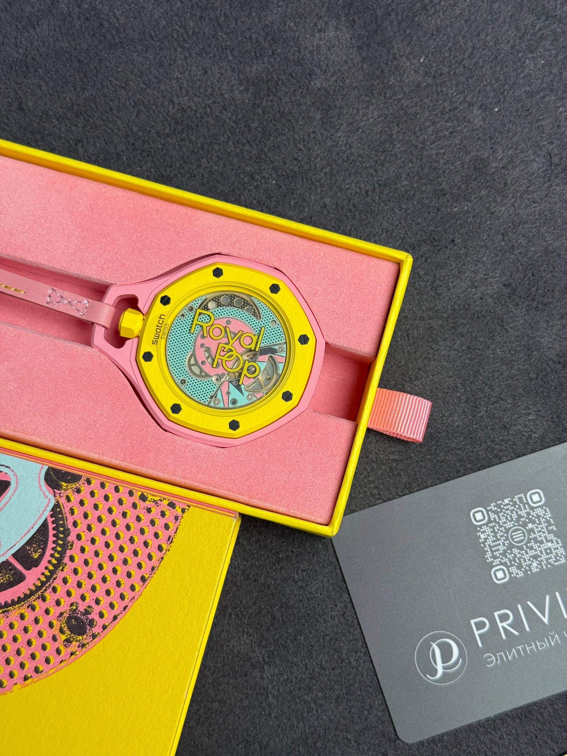 Swatch wristwatch in pink and yellow packaging; yellow bezel, pink band, in an open pink foam-lined box.