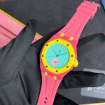 Bright pink Swatch wristwatch with turquoise dial being held by a gloved hand.