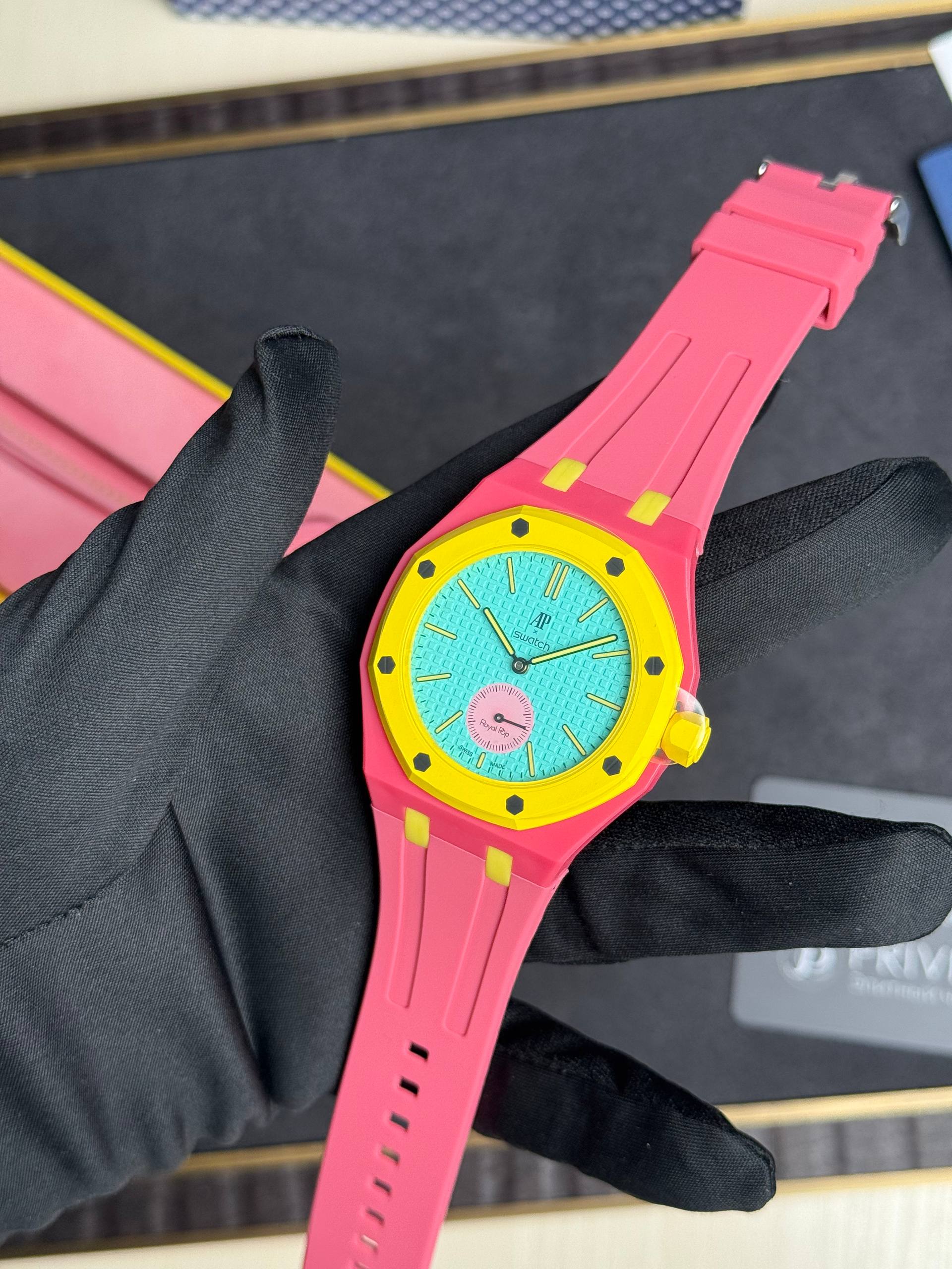Bright pink Swatch wristwatch with turquoise dial being held by a gloved hand.