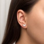 Butterfly-shaped stud earring in white with a gold beaded edge on a model's earlobe, brunette hair tucked behind the ear