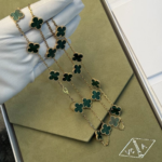 Gold chain necklace with emerald green clover pendants outlined in gold, resting on a green velvet jewelry box.