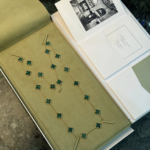 Gold chain necklace with green clover charms arranged in a pale green jewelry box with an open book nearby.