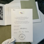 Person wearing a white glove holding an authentication certificate and a Van Cleef & Arpels document with a seal visible. A green booklet rests in the background.