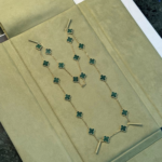 Gold chain necklace with green four-leaf-clover links laid on a beige display surface.