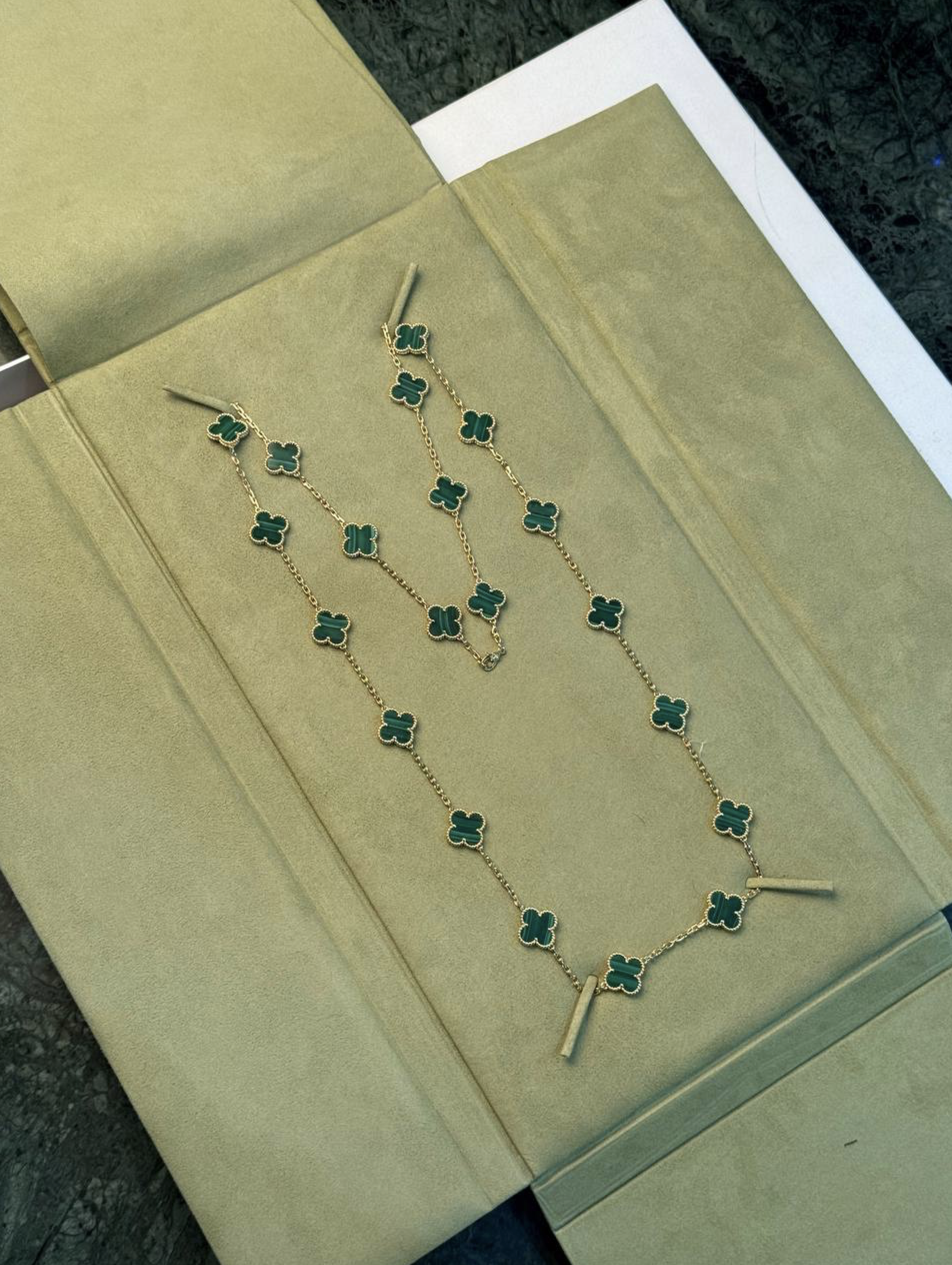 Gold chain necklace with green four-leaf-clover links laid on a beige display surface.