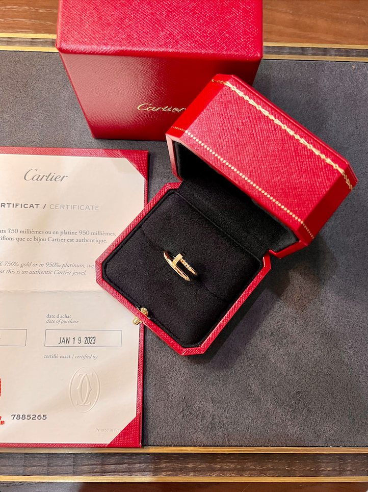 Gold ring in a red Cartier box on a display, with a certificate nearby.