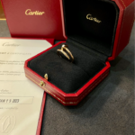 Gold Cartier ring in an open black velvet jewelry box with the Cartier logo, inside a red presentation box with stitching.